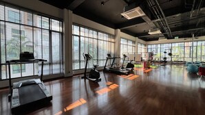 A spacious gym with multiple exercise machines, large windows, and a wooden floor. - Triple J Suite (Si Racha)
