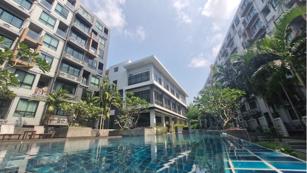 A modern building with a swimming pool, surrounded by greenery and other residential buildings. - Triple J Suite (Si Racha)