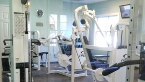 Un gimnasio con diferentes máquinas de ejercicio, un reloj en la pared y un ventanal que deja entrar luz natural.