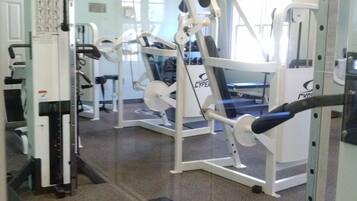 Une salle de sport équipée de divers appareils d’exercice, avec une horloge au mur et une fenêtre laissant entrer la lumière naturelle.