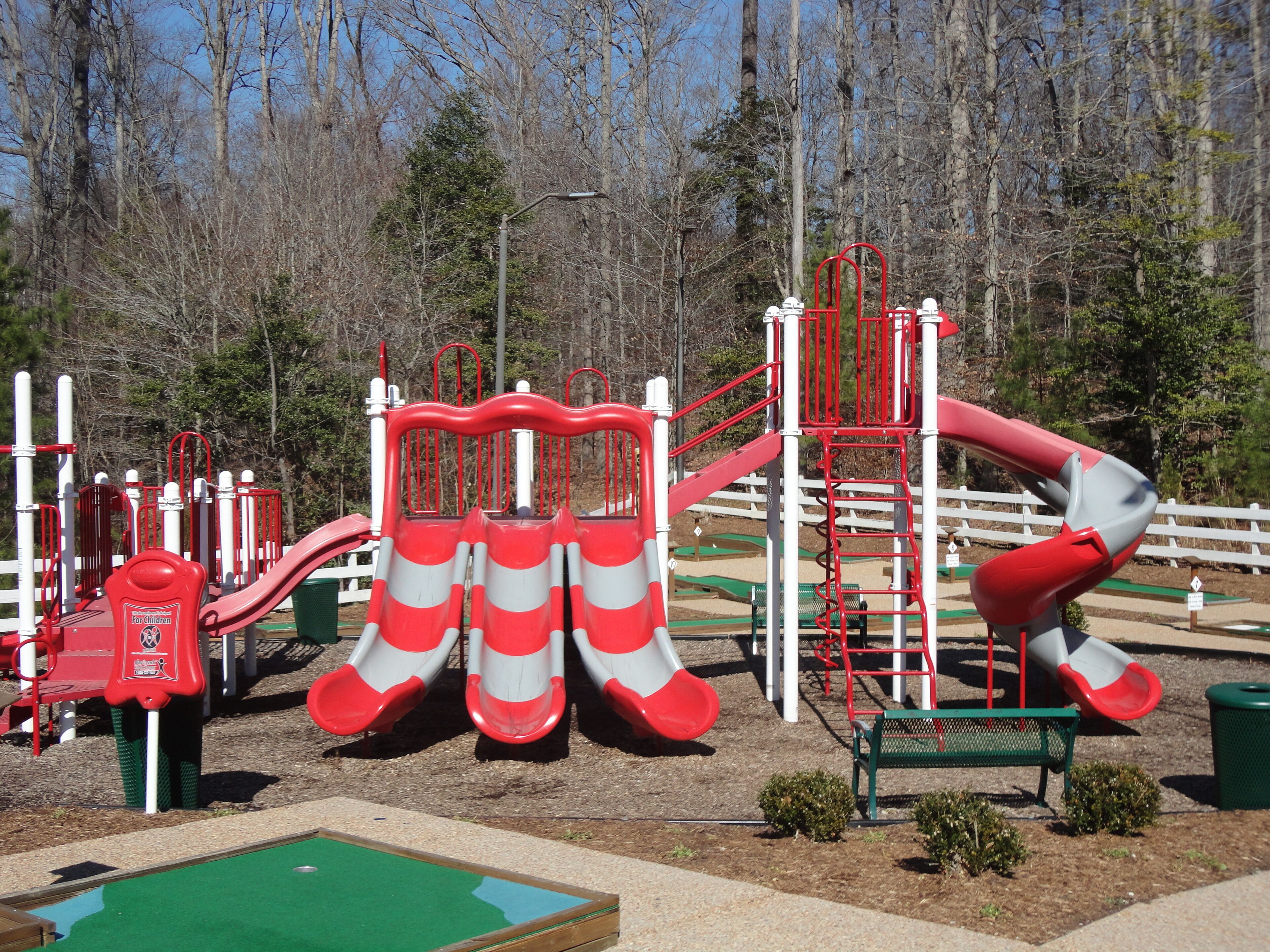A playground with red and white slides, climbing structures, and a green play area.