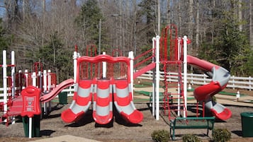 A playground with red and white slides, climbing structures, and a green play area.