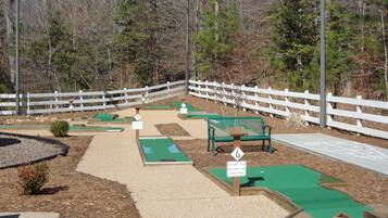 Un parcours de mini-golf avec des trous numérotés, un banc vert et une clôture blanche.