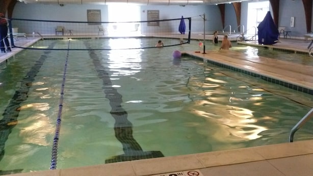 Una piscina interior con carriles delimitados, vigas de madera en el techo y suelo de baldosas.