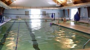 Une piscine intérieure avec des couloirs bien délimités, des poutres en bois au plafond et un sol carrelé.