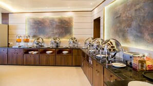 Una barra de desayuno moderna con estaciones de comida tipo buffet, incluyendo dispensadores de jugo y una tostadora.