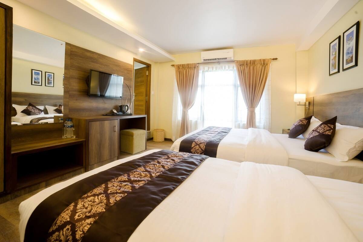 A hotel room with two beds, a TV, a desk, and a mirror.
