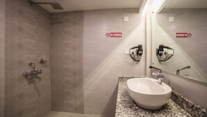 Un baño con ducha, lavabo, espejo y dos letreros de prohibido fumar.