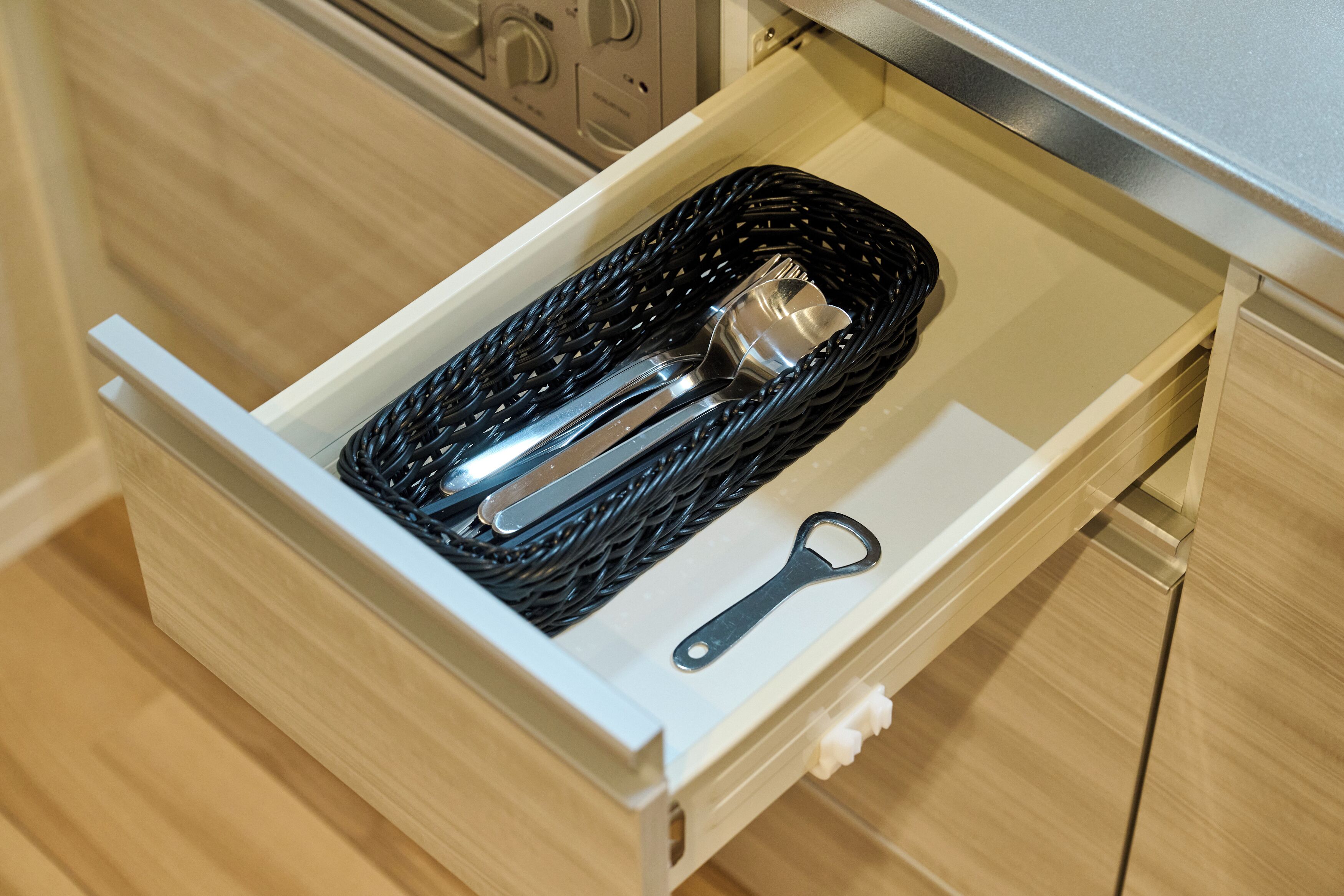 Un cajón con una cesta negra tejida que contiene un recipiente metálico y un abridor de metal.