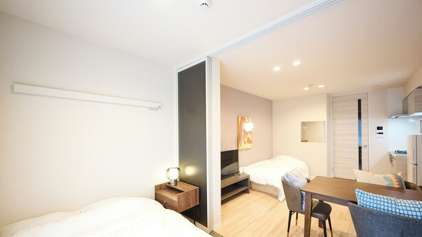 A modern hotel room with a bed, a desk, a chair, a television, and a small kitchenette. - ShaMaison richelive Yoshizuka by Tranova (Fukuoka)