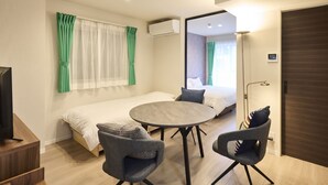 A hotel room with a bed, a round table, two chairs, a TV, and a mirror. - ShaMaison richelive Yoshizuka by Tranova (Fukuoka)