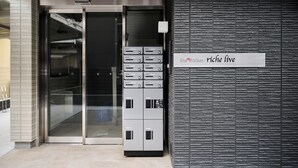 A modern building entrance with a glass door, a sign reading 'Sham Maison riche live,' and a series of control panels. - ShaMaison richelive Yoshizuka by Tranova (Fukuoka)