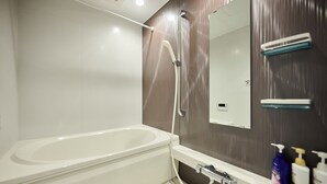 A modern bathroom with a bathtub, a shower, a mirror, and a shelf with toiletries. - ShaMaison richelive Yoshizuka by Tranova (Fukuoka)