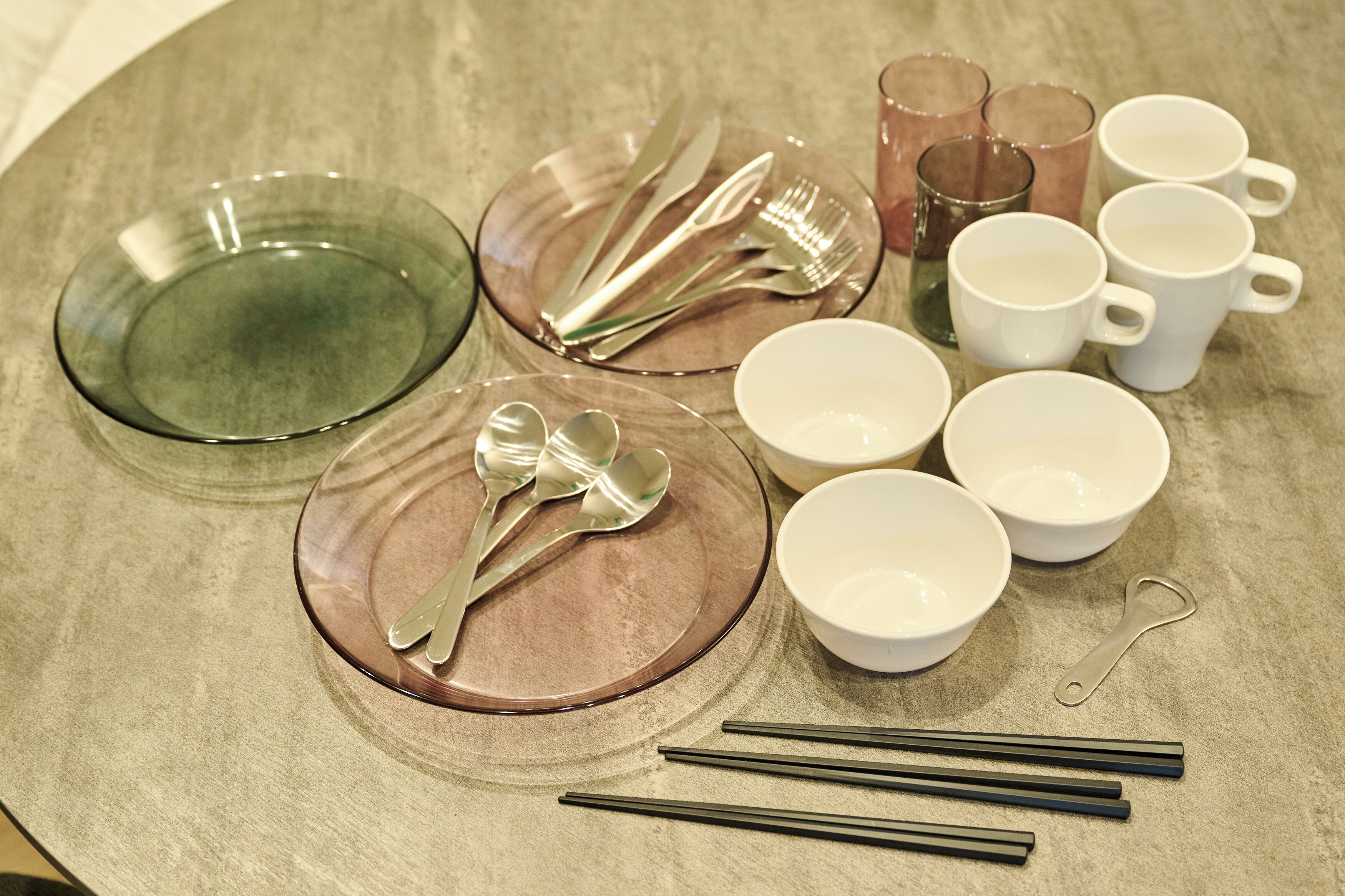 A table set with clear glass plates, silverware, white cups, and chopsticks.