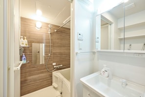 Ein modernes Badezimmer mit einer Duschkabine aus Holz, einem weißen Waschbecken mit Spiegel darüber und Toilettenartikeln auf dem Waschbecken.