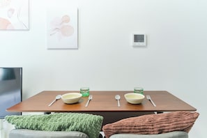 A dining table with two bowls, spoons, and green glasses, a thermostat, and a green knitted blanket on a chair.