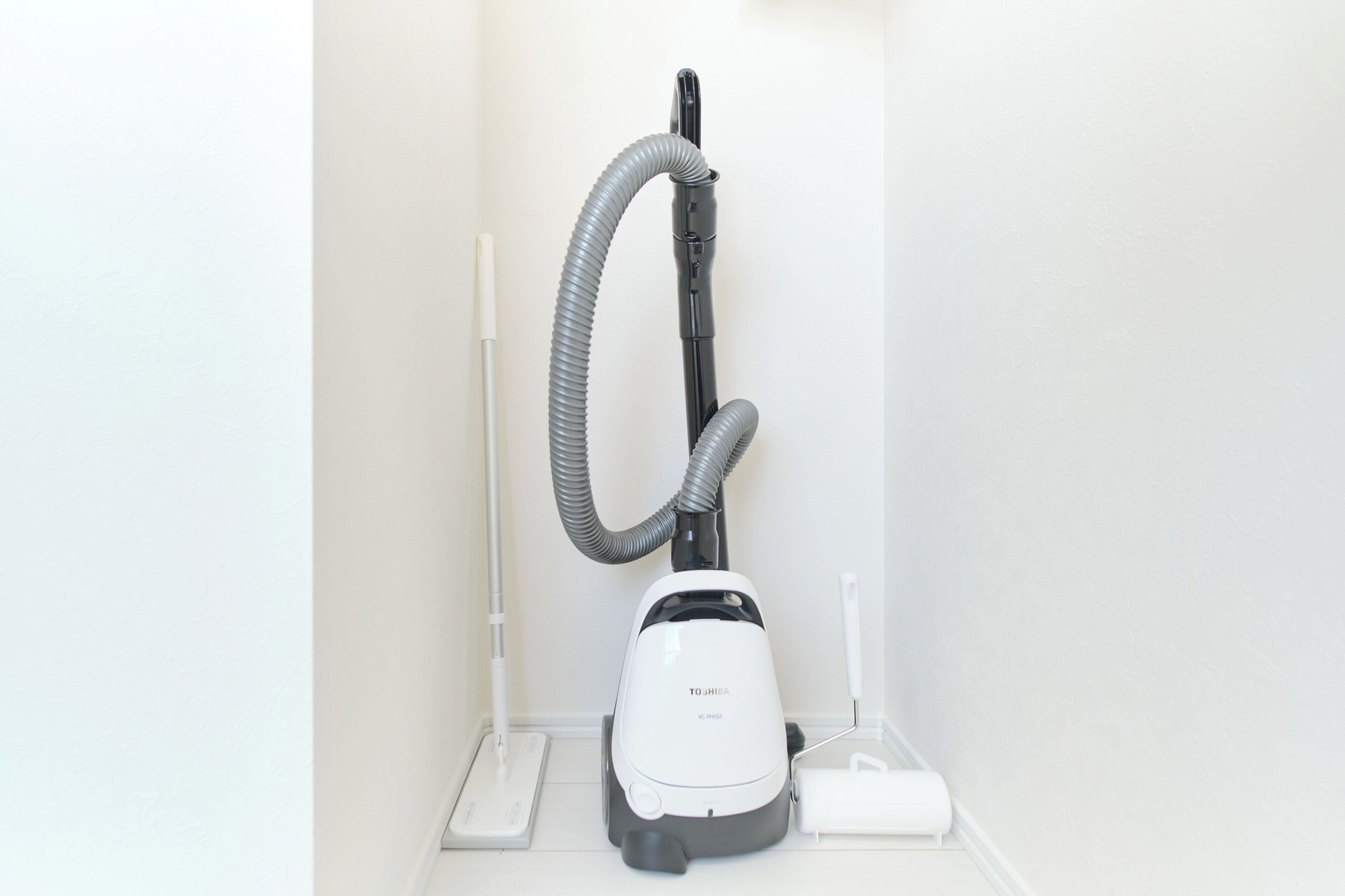 Een stofzuiger in een hoek van een kamer met een witte vloer en witte wanden.
