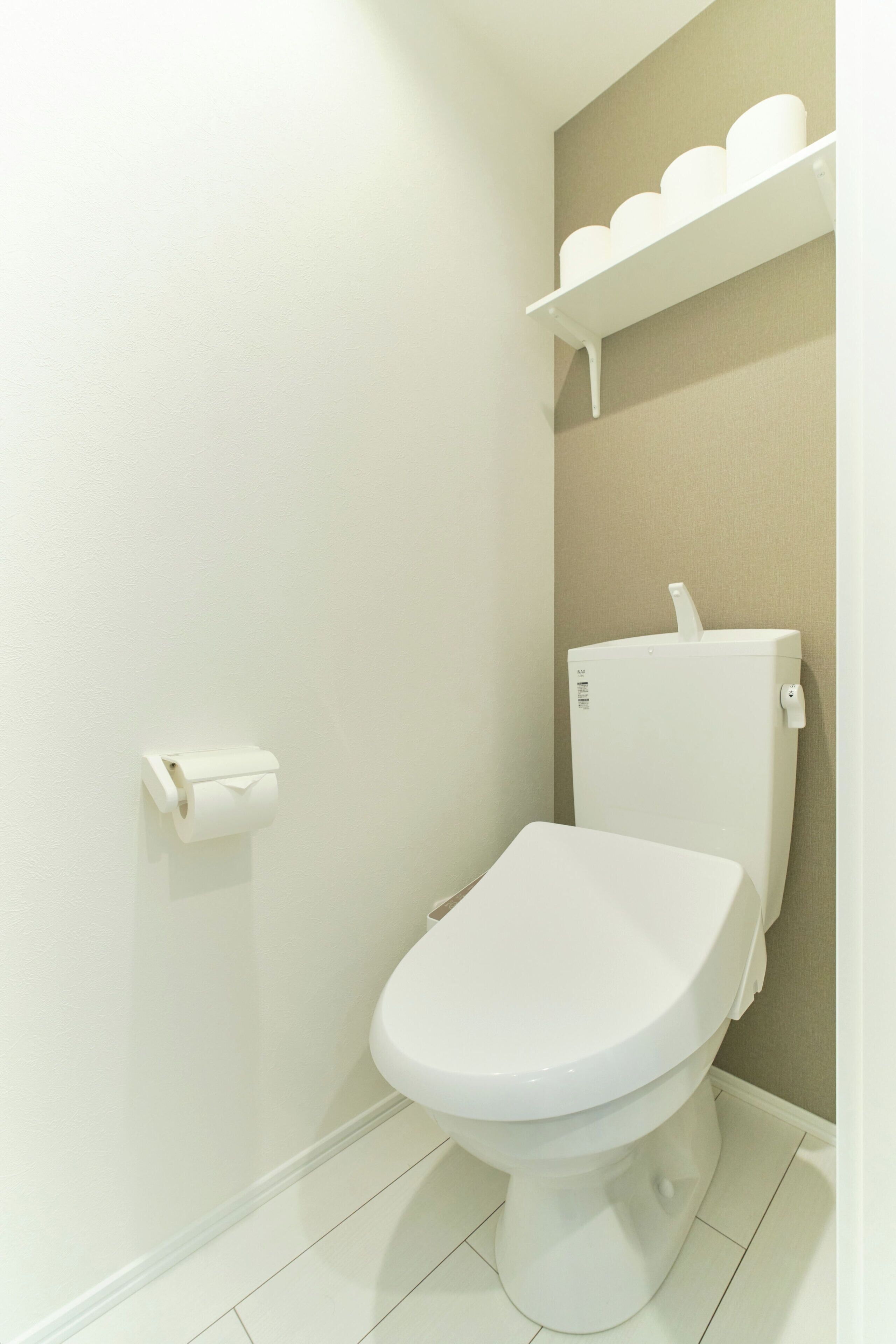 A bathroom with a toilet, a roll of toilet paper, and a shelf above the toilet.