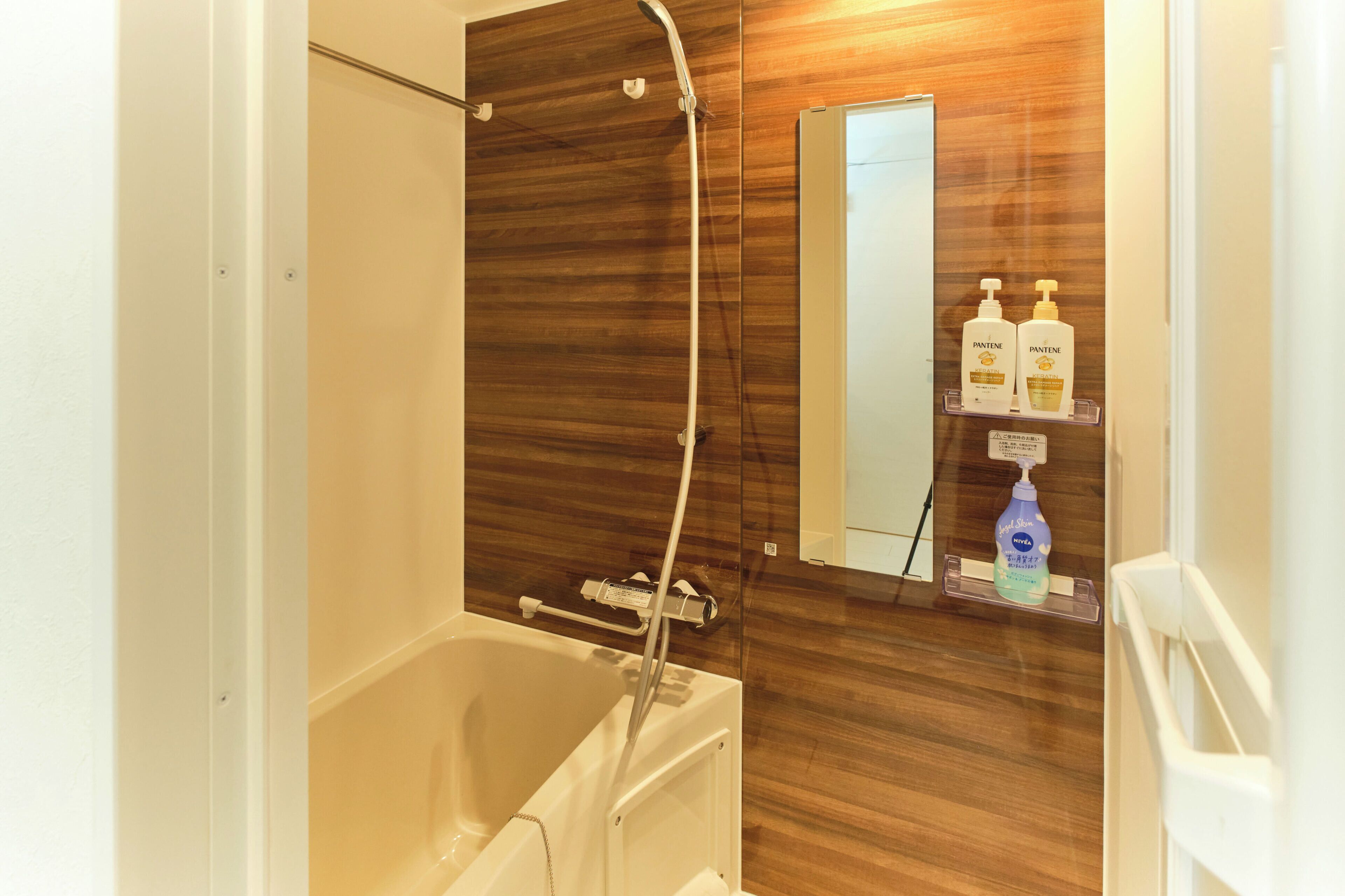 A bathroom with a bathtub, a wooden wall, a mirror, and a shelf with toiletries.