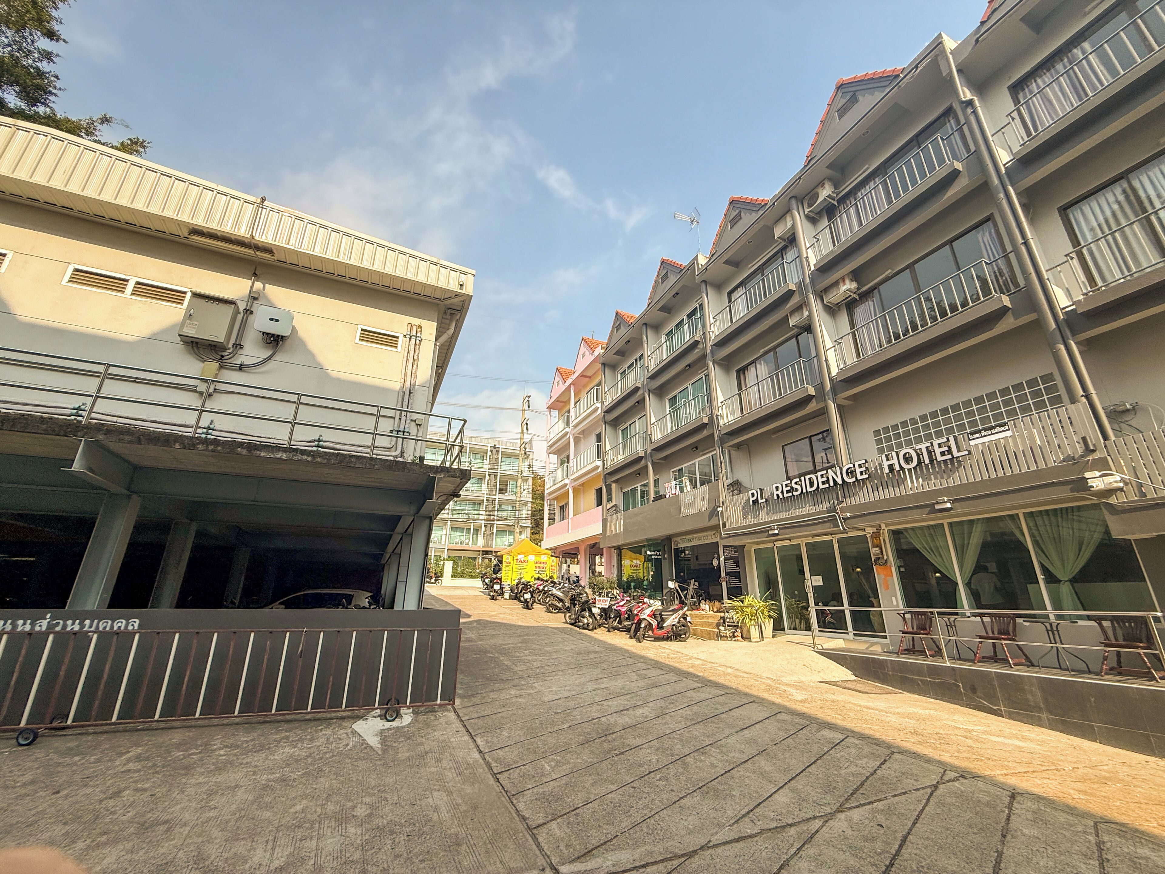 A hotel with a sign reading 'PL RESIDENCE HOTEL,' a covered area with a railing, and a row of parked motorcycles.