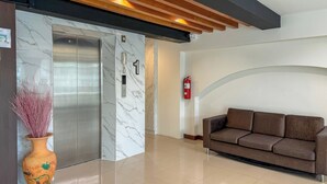 Un vestíbulo moderno con un ascensor de mármol, techo de madera, sofá de cuero marrón y extintor.