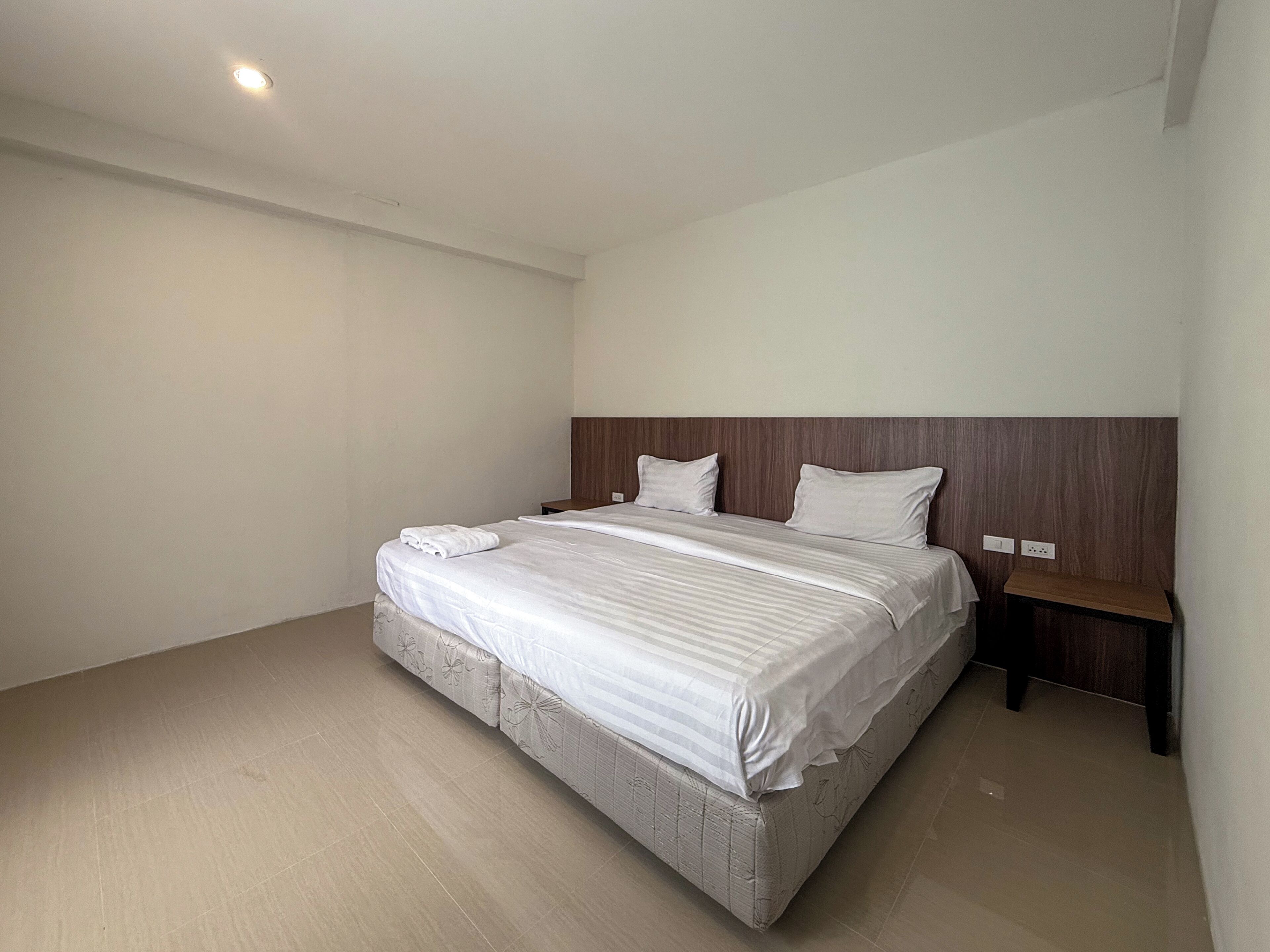 A modern hotel room with a large bed, wooden headboard, and a nightstand.