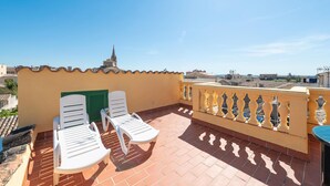 A terrace with two white lounge chairs, a yellow balustrade, and a view of the cityscape.