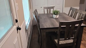 A dining area with a wooden table, chairs, a potted plant, and a clock on the wall. - The Delta Dream Cottage- minutes from Memphis (Horn Lake)