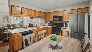 A modern kitchen with wooden cabinets, stainless steel appliances, a dining area with a wooden table, and a living area with a sofa and a TV. - The Delta Dream Cottage- minutes from Memphis (Horn Lake)