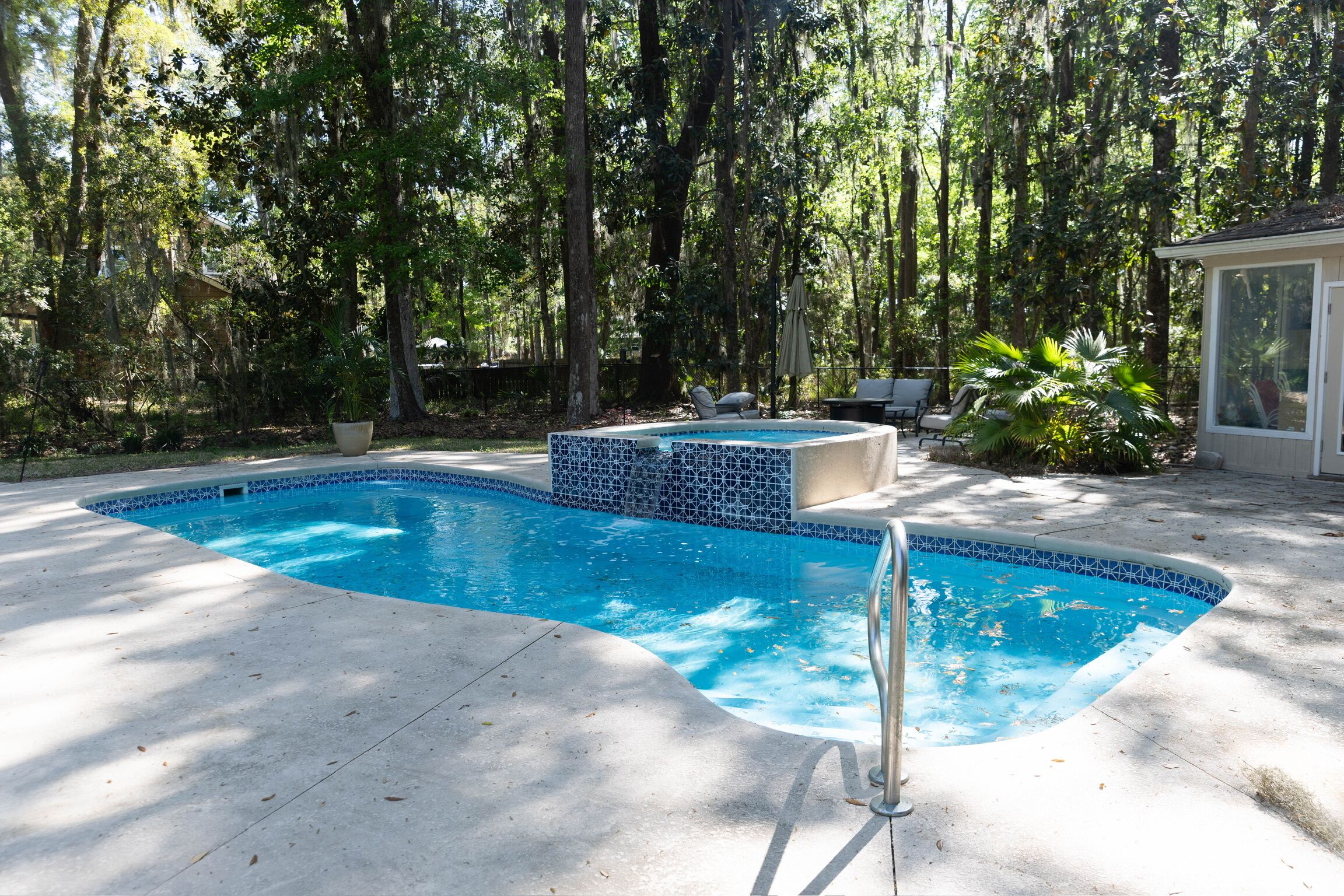 A swimming pool with a tiled edge, surrounded by a concrete deck, with trees in the background.