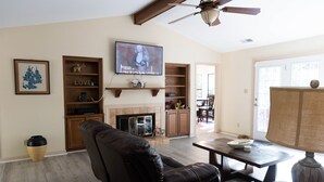 Una sala de estar con sofá de cuero, televisor montado en la pared, chimenea y comedor con mesa y sillas.