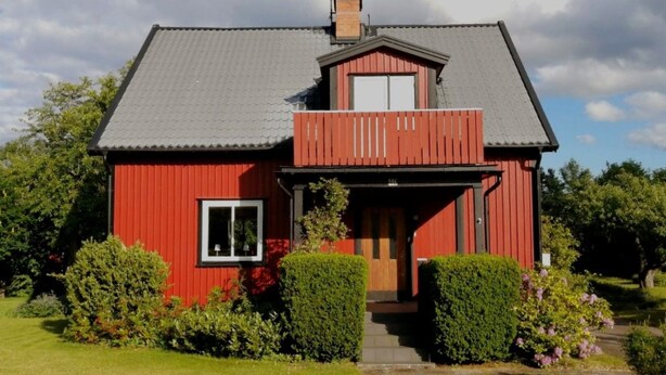 Ein rotes Haus mit grauem Dach, Schornstein, Balkon und kleinem Garten.