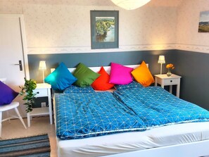 A bedroom with a bed, colorful pillows, a nightstand with a lamp, a framed picture on the wall, and a plant. - Buntes Schwedenhaus Lillebror by Interhome (Fågelfors)