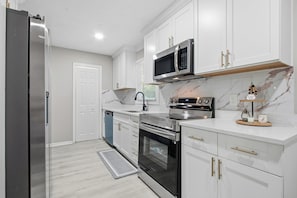 A modern kitchen with white cabinets, stainless steel appliances, and a marble backsplash.