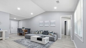 Ein modernes Wohnzimmer mit grauem Sofa, einem Couchtisch und einem Essbereich mit Stühlen und Tisch.