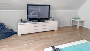 A room with a flat-screen TV on a white TV stand, a small white side table with a lamp, and a bean bag chair.