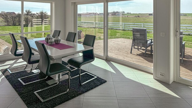 A modern dining area with a table and chairs, large windows, and a view of the outdoors.