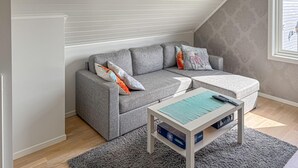 A grey sectional sofa with colorful pillows, a small white table with a remote control, and a grey carpet.