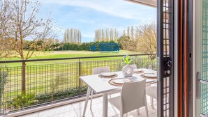 Ein Balkon mit Esstisch, Blick auf einen Golfplatz und eine Tür mit Metallbeschlägen.