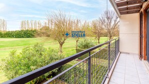 Ein Balkon mit Blick auf ein grünes Feld und Bäume, einem Metallgeländer und einem Gebäudeeingang.
