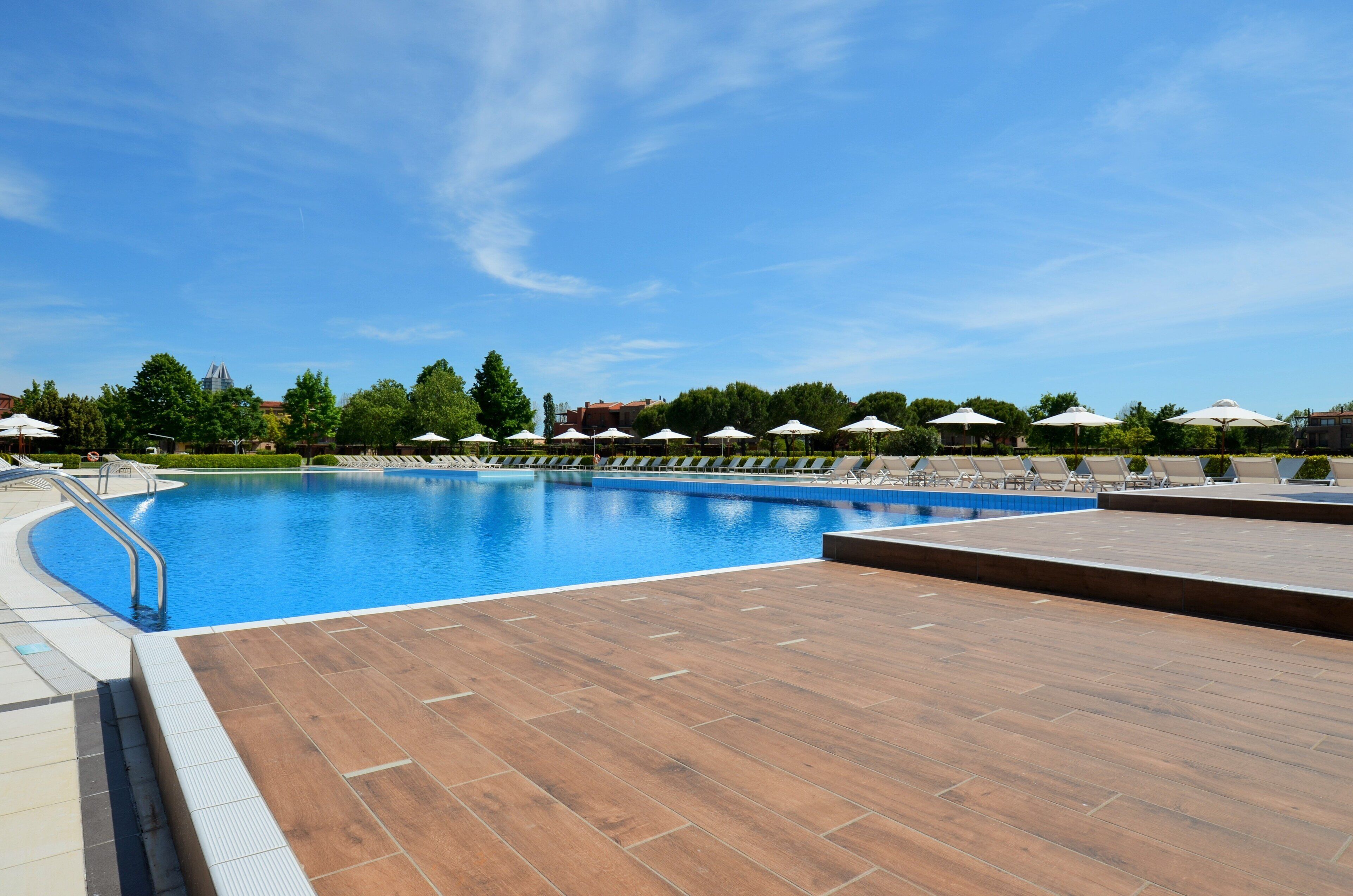 Une piscine dotée d’une terrasse en bois, entourée de parasols et de chaises longues.