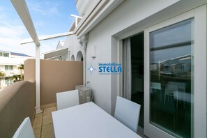 A balcony with white wicker furniture, a glass door, and a logo for 'immobiliare STELLA'. - WAVE2 [residence pool+#trilocale#] (Lido di Jesolo)