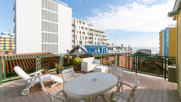 Terraza en la azotea con mobiliario exterior y vistas a la ciudad, con un cartel que dice 'immobiliare STELLA'.