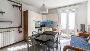Una cocina moderna con armarios blancos, una mesa de comedor con sillas, una cama con colcha azul y un balcón con vistas.