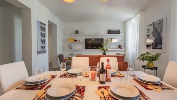 A dining area with a table set for four, a television in the background, and a sofa. - Great Opera at Via Palermo (Roma)
