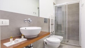 A modern bathroom with a large white sink, a toilet, and a glass shower enclosure. - Great Opera at Via Palermo (Roma)