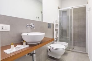 A modern bathroom with a large white sink, a toilet, and a glass shower enclosure. - Great Opera at Via Palermo (Roma)