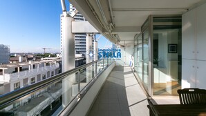 Un balcon doté d’une balustrade en verre, d’un banc en bois et offrant une vue sur des immeubles et une grande roue.
