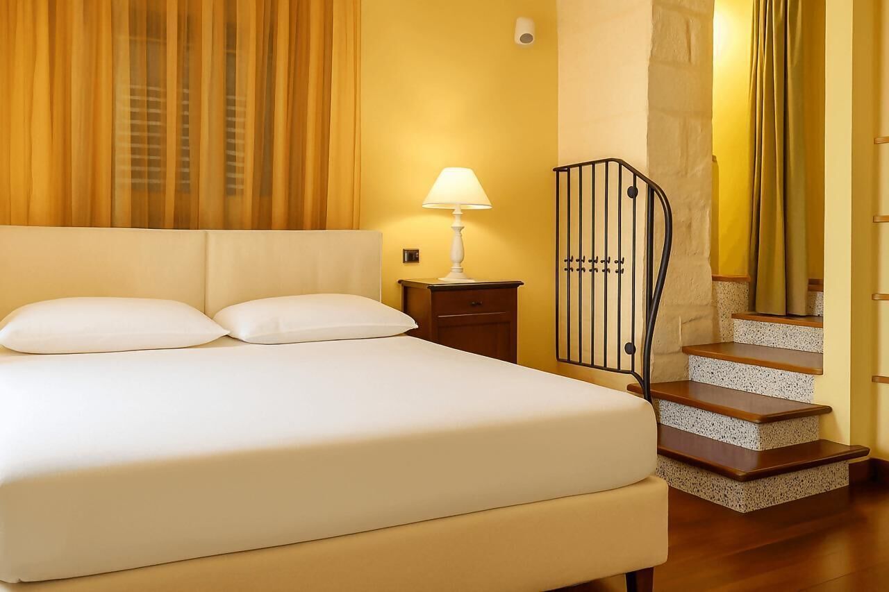 Una habitación de hotel con cama, mesita de noche, lámpara y escalera.
