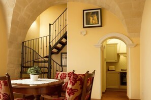 Un espace repas comprenant une table ronde, des chaises, une plante en pot, un escalier et une arche menant à la cuisine.
